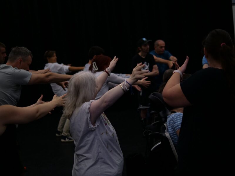 http://A%20dynamic%20image%20of%20a%20workshop.%20Workshop%20participants%20all%20outstretch%20their%20arms,%20reaching%20upwards%20and%20outwards%20in%20different%20directions.
