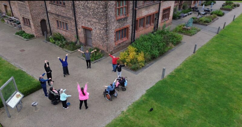 http://In%20the%20gardens%20of%20Ordsall%20Hall,%20an%20aerial%20view%20of%20DIY%20Theatre%20and%20Uncurbed%20Collective%20artists%20in%20a%20circle,%20reach%20towards%20the%20sky%20in%20synchronisation.