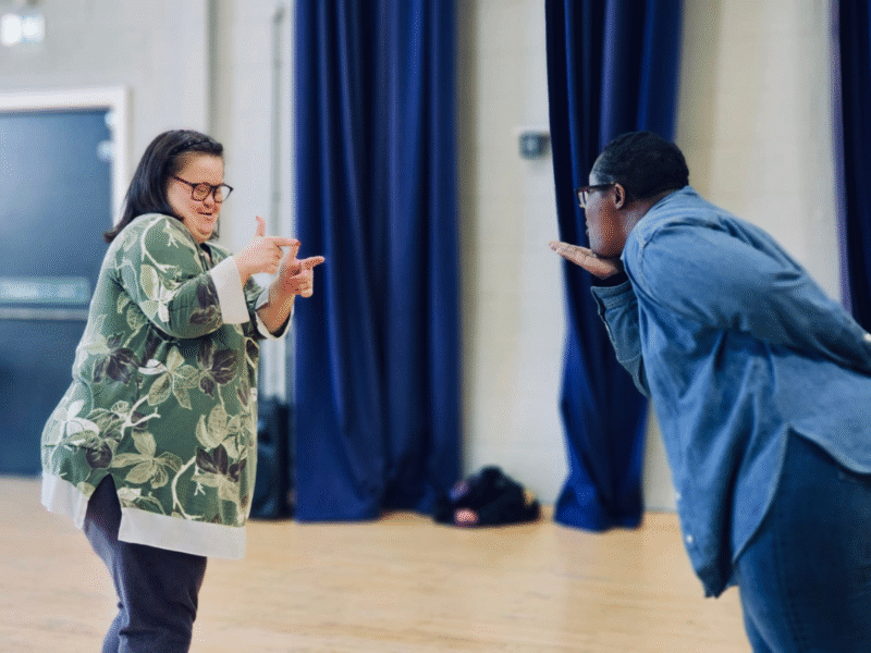 http://Two%20workshop%20participants%20playfully%20gesture%20towards%20each%20other.%20One%20blows%20a%20kiss,%20the%20other%20cooly%20points%20at%20them.